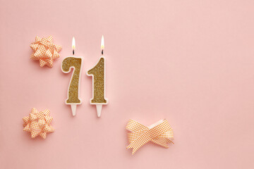 Fototapeta na wymiar Candles with the number 71 on a pastel pink background with festive decor. Happy birthday candles. The concept of celebrating a birthday, anniversary, important date, holiday. Copy space. banner