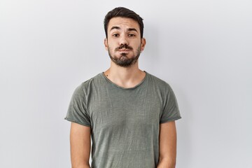 Young hispanic man with beard wearing casual t shirt over white background puffing cheeks with funny face. mouth inflated with air, crazy expression.