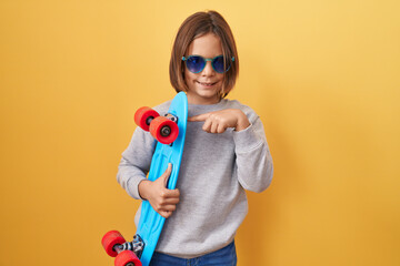 Little hispanic boy wearing sunglasses holding skate smiling happy pointing with hand and finger