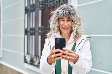 Middle age woman smiling confident using smartphone at street
