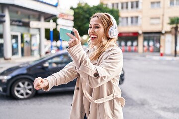Fototapeta premium Young blonde woman listening to music and dancing at street