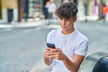 Fototapeta na wymiar Young hispanic teenager using smartphone with relaxed expression at street