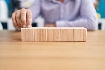 Young hispanic man business worker sitting on table with wooden cubes at office