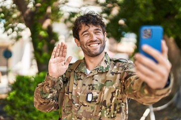 Hispanic young man wearing camouflage army uniform doing video call looking positive and happy standing and smiling with a confident smile showing teeth