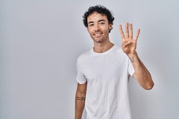 Hispanic man standing over isolated background showing and pointing up with fingers number four while smiling confident and happy.