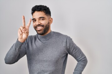 Hispanic man with beard standing over white background smiling looking to the camera showing...