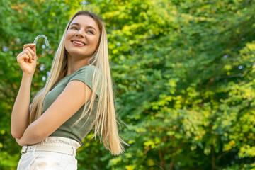 Girl in green t-shirt holding an invisible teeth aligner while smiling outdoors