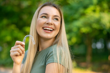 Happy girl puts a dental retainer on her teeth, she stands on a green background. Orthodontist. Dental tray. Retainer. Place for an inscription. - 597280854