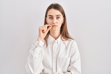 Young caucasian woman standing over isolated background mouth and lips shut as zip with fingers....