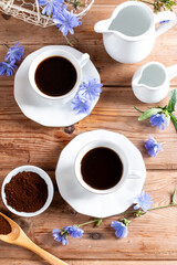 Healthy hot chicory drink in the cup , crushed chicory root in small white bowl and milk in glass jug on a table. Top view
