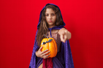 Little hispanic girl wearing witch halloween costume pointing with finger to the camera and to you, confident gesture looking serious