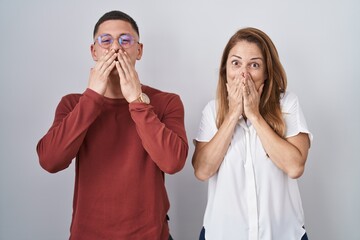 Mother and son standing together over isolated background laughing and embarrassed giggle covering...