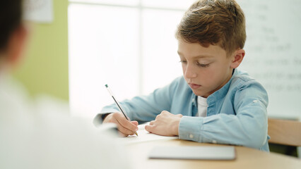 Adorable caucasian boy student writing on notebook studying at classroom