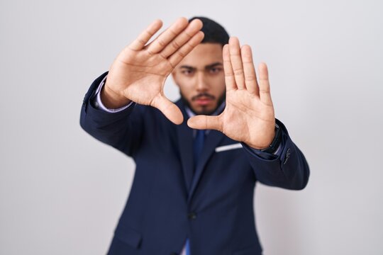 Young hispanic man wearing business suit and tie doing frame using hands palms and fingers, camera perspective