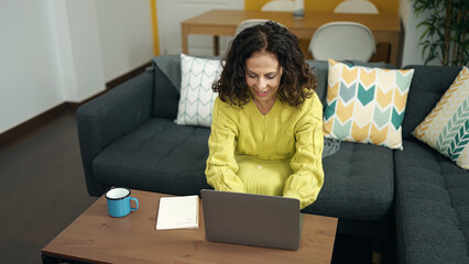 Middle age hispanic woman using laptop sitting on sofa at home