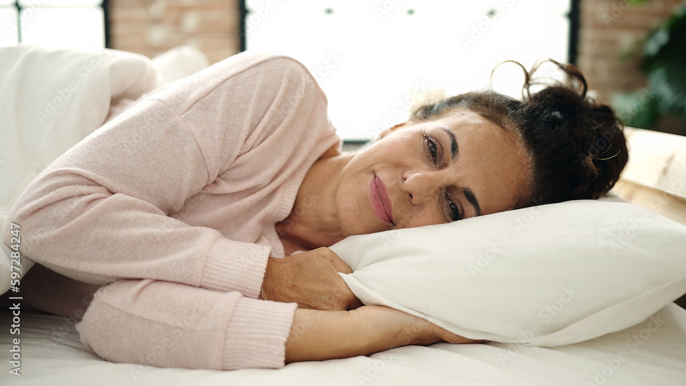 Sticker middle age hispanic woman smiling confident lying on bed at bedroom