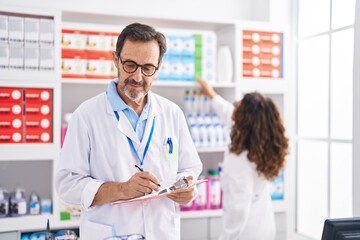 Man and woman pharmacists writing on document working at pharmacy