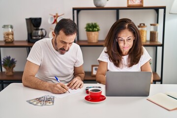 Middle age man and woman couple accounting family economy sitting on table at home