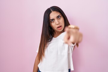 Young arab woman standing over pink background pointing displeased and frustrated to the camera,...