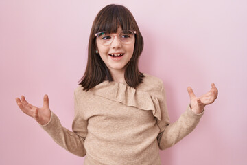 Little hispanic girl wearing glasses celebrating mad and crazy for success with arms raised and...