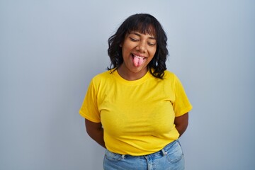 Hispanic woman standing over blue background sticking tongue out happy with funny expression. emotion concept.