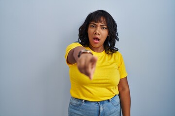 Hispanic woman standing over blue background pointing displeased and frustrated to the camera,...