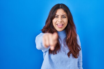 Fototapeta premium Hispanic young woman standing over blue background pointing displeased and frustrated to the camera, angry and furious with you