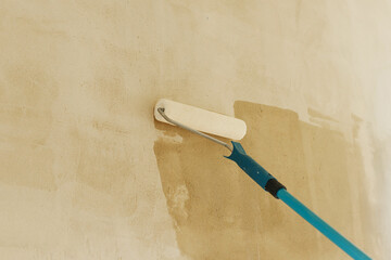 Worker priming walls in new building. Roller brush with prime covering plaster walls. Construction...