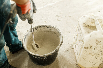 Worker mixing gypsum plaster with water for plastering walls. Construction of house and home renovation concept. Close up of bucket with stucco mix and handyman hands - obrazy, fototapety, plakaty