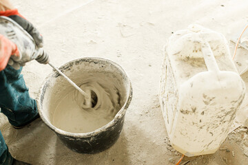 Worker mixing gypsum plaster with water for plastering walls. Construction of house and home renovation concept. Close up of bucket with putty mix and handyman hands