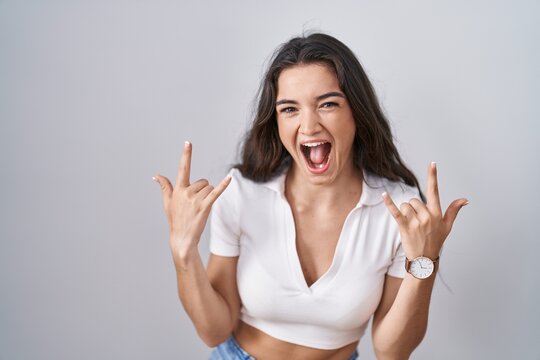 Young teenager girl standing over white background shouting with crazy expression doing rock symbol with hands up. music star. heavy music concept.