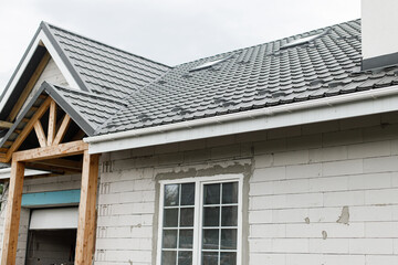 Stylish building with unfinished facade, white windows, modern black roof and wooden porch. Modern new farmhouse building exterior.
