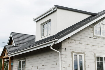 Stylish building with unfinished facade, white windows, modern black roof and dormer. Modern new farmhouse building exterior.