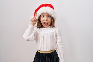 Little hispanic girl wearing christmas hat smiling with an idea or question pointing finger up with happy face, number one