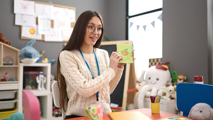 Young beautiful hispanic woman preschool teacher teaching vocabulary lesson at kindergarten