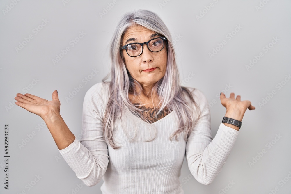 Poster Middle age woman with grey hair standing over white background clueless and confused expression with arms and hands raised. doubt concept.