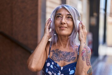 Middle age grey-haired woman smiling confident listening to music at street