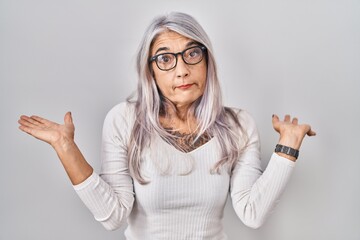 Middle age woman with grey hair standing over white background clueless and confused expression...