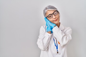 Middle age woman with grey hair wearing scientist robe sleeping tired dreaming and posing with hands together while smiling with closed eyes.