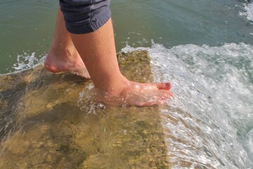 Feet of a young man barefoot in the water on a concrete slab. Side sun illuminates