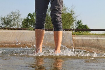 Feet of a young man barefoot in the water on a concrete slab. Side sun illuminates water splash
