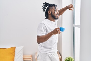 Fototapeta na wymiar African american woman drinking coffee standing at bedroom