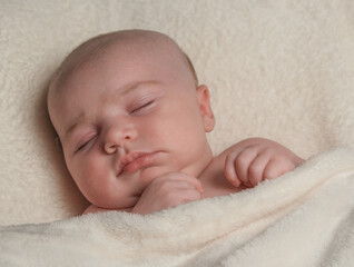 Portrait of newborn baby girl sleeping on her back, covered with a cream blanket.