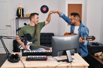 Two men musicians smiling confident bump fists at music studio