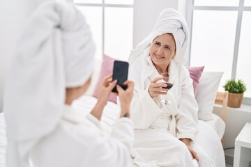 Mother and daughter make photo by the smartphone drinking glass of wine at bedroom