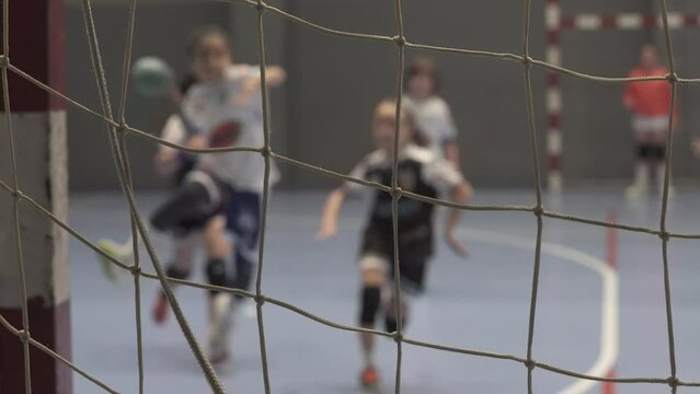 4K footage of girls playing handball and finishing the play in goal in a defocused shot from behind the goal net
