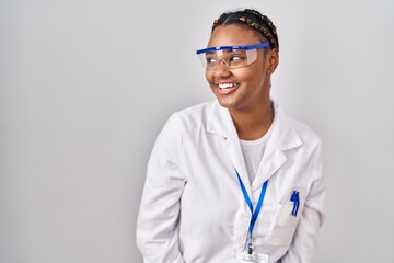 African american woman with braids wearing scientist robe looking away to side with smile on face, natural expression. laughing confident.