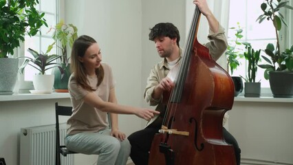Handsome man teaches a woman to play the double bass. 