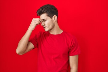 Young hispanic man standing over red background tired rubbing nose and eyes feeling fatigue and headache. stress and frustration concept.