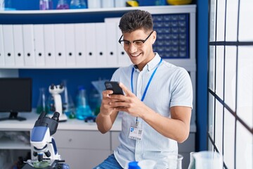 Young hispanic man scientist using smartphone working at laboratory
